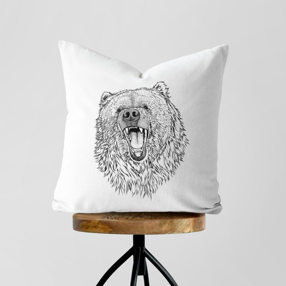 White pillow cover printed with a detailed black ink portrait of a roaring Kodiak bear facing forward, on a wooden stool.