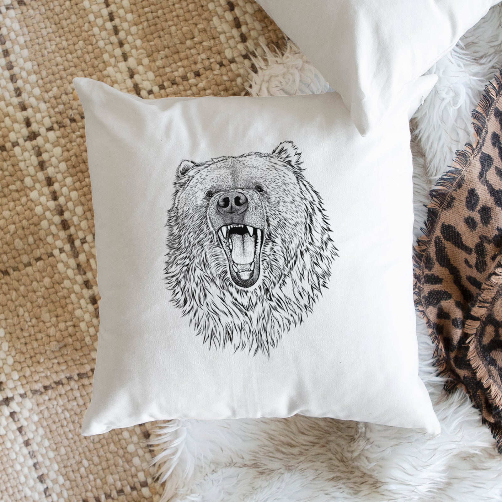 White pillow cover printed with a detailed black ink portrait of a roaring Kodiak bear facing forward, on a bench beside plants.