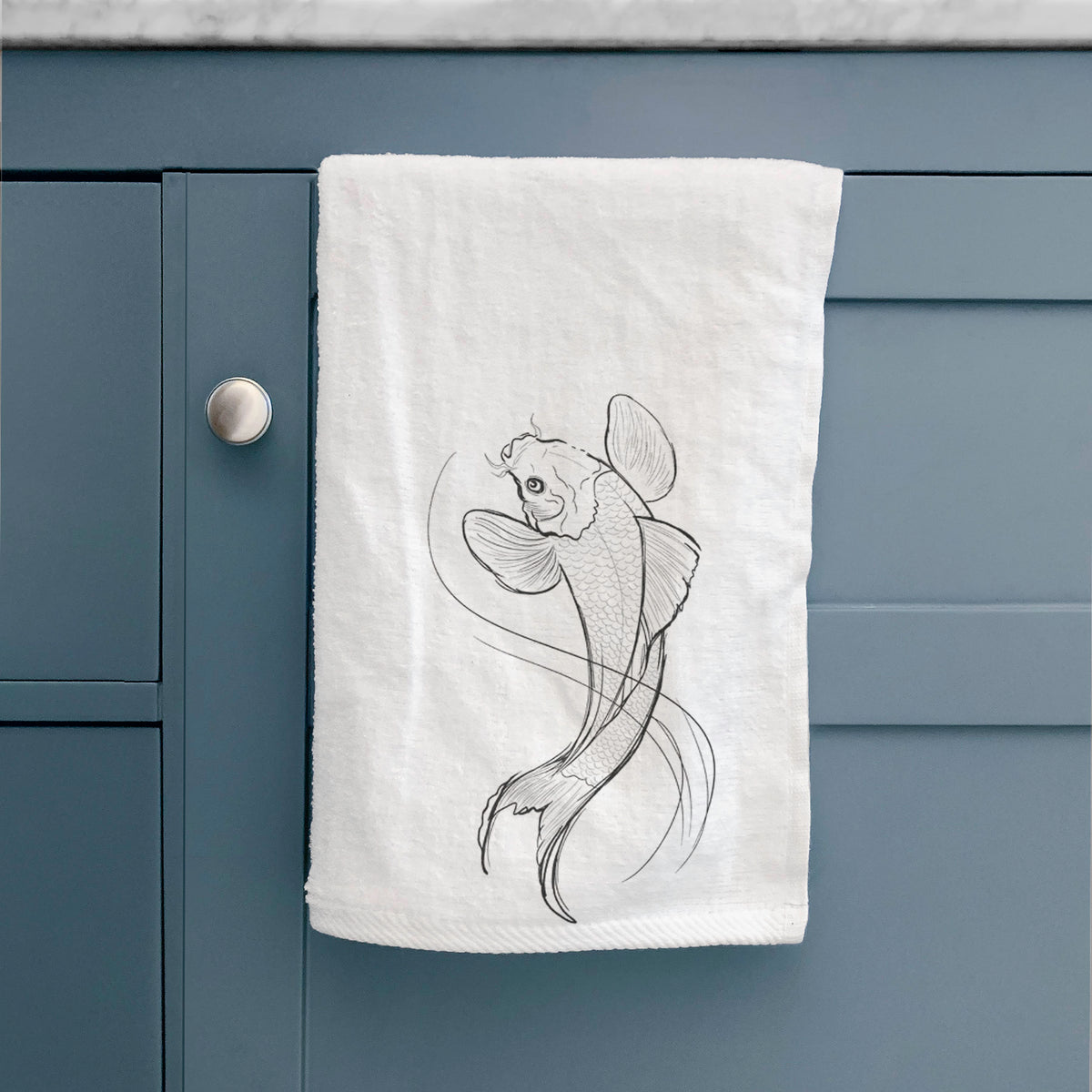 White hand towel printed with a black ink line drawing of a koi fish swimming with flowing fins, hanging on a cabinet door.