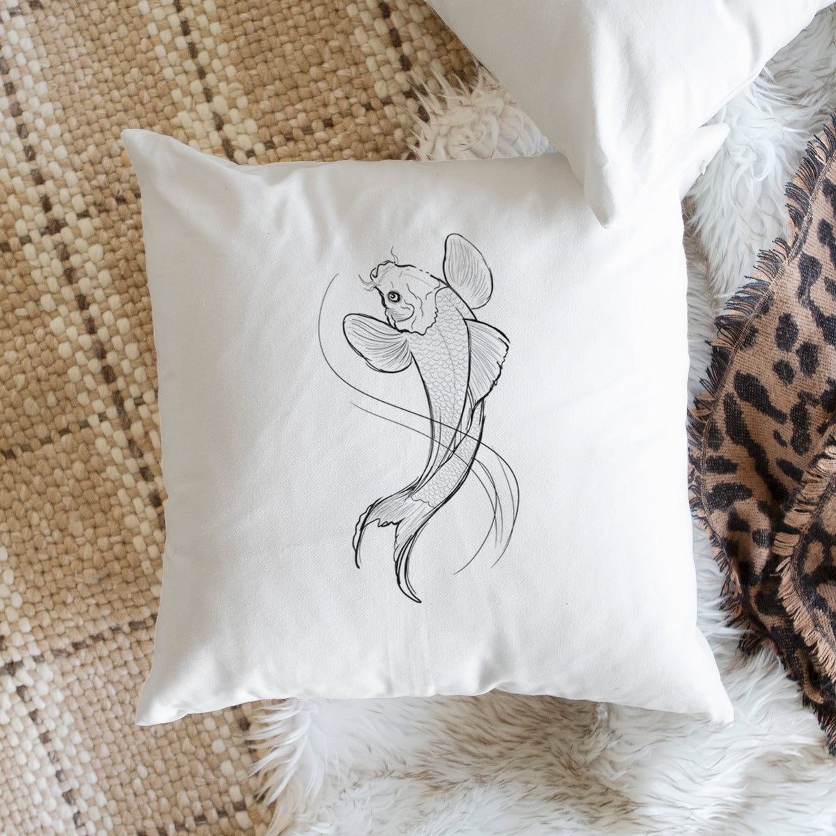 White pillow cover printed with a black ink line drawing of a koi fish swimming with flowing fins, on a woven chair.