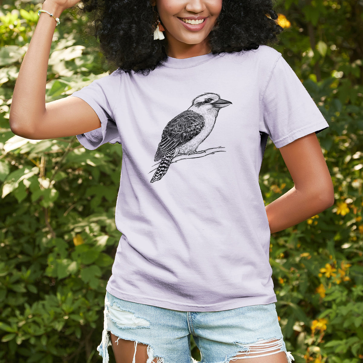 Woman wearing a Comfort Colors t-shirt printed with a detailed black ink sketch of a kookaburra perched on a branch, outdoors.