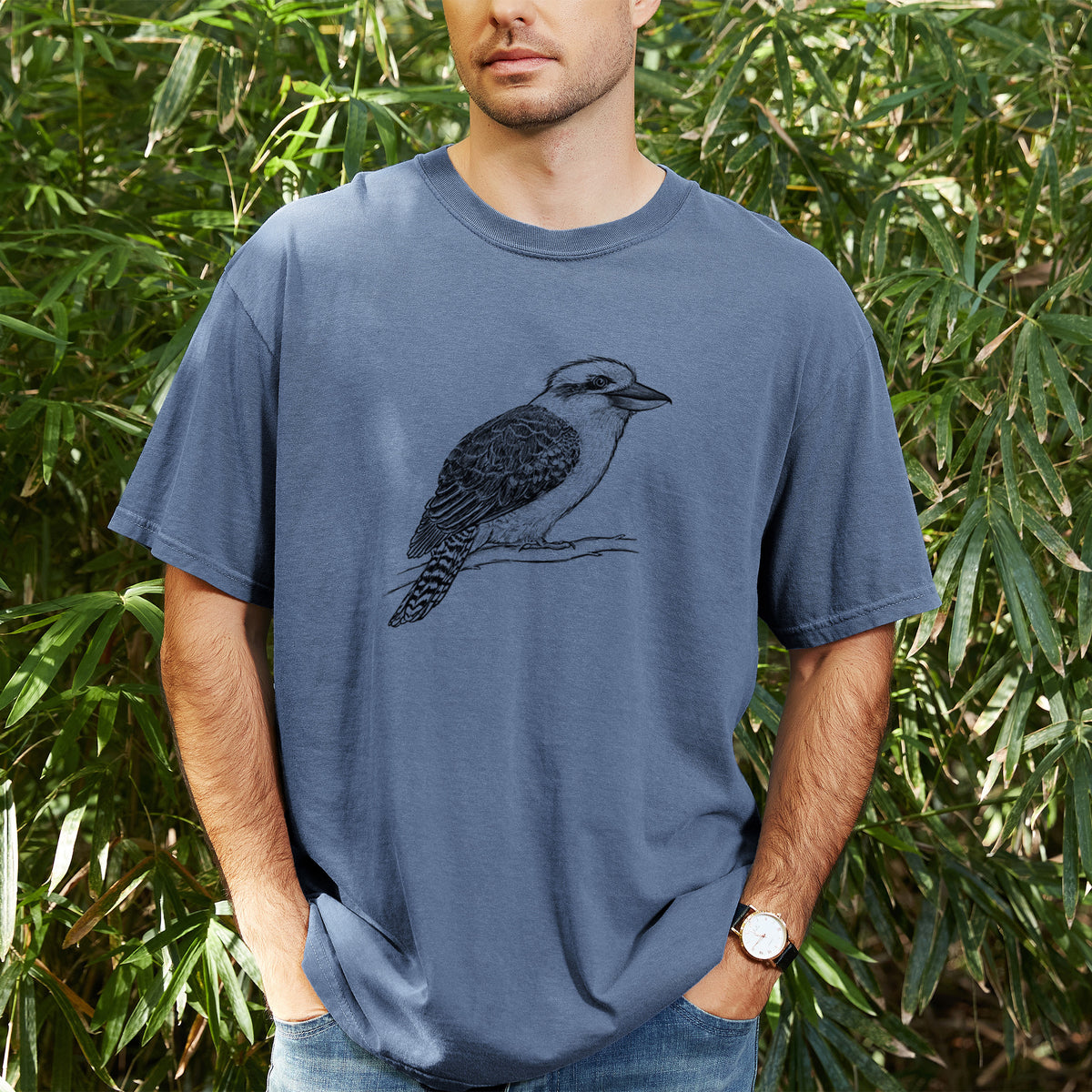 Man wearing a Comfort Colors t-shirt printed with a detailed black ink sketch of a kookaburra perched on a branch, outdoors.