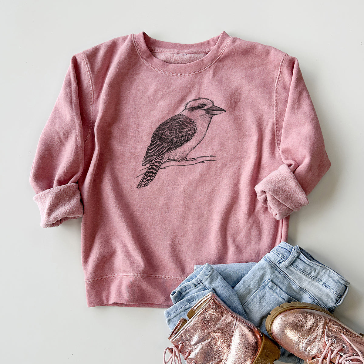 Youth crewneck sweatshirt printed with a detailed black ink sketch of a kookaburra perched on a branch, styled flat with jeans and boots.