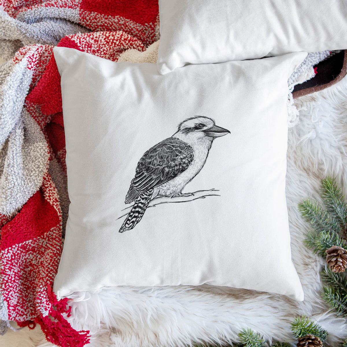 White pillow cover printed with a detailed black ink sketch of a kookaburra perched on a branch, on a woven chair.