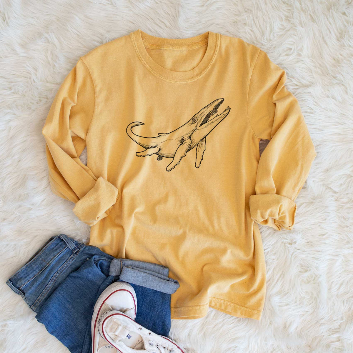 Golden wheat yellow Comfort Colors long sleeve shirt printed with a black ink illustration of a Kronosaurus marine reptile swimming, shown in a lifestyle photo.
