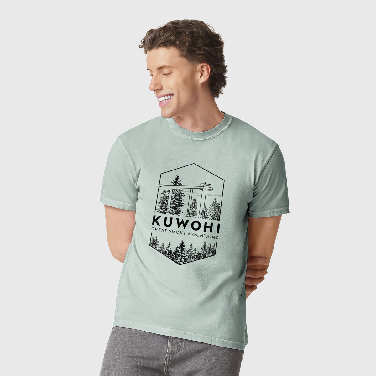 Man wearing a Comfort Colors t-shirt printed with a black line art badge of the Kuwohi observation tower above pine trees, with the words Kuwohi, Great Smoky Mountains.