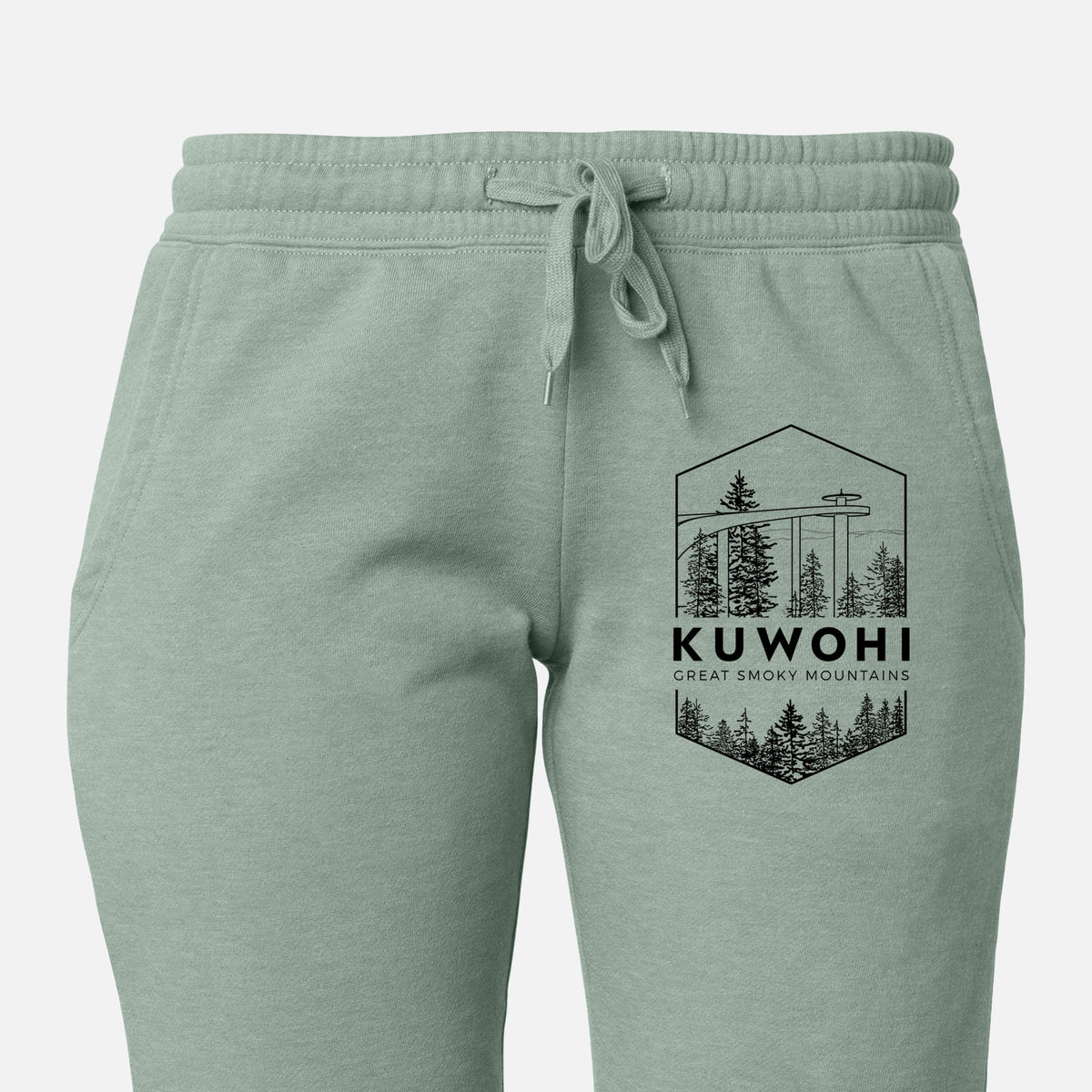 Front of sage green Cali Wave sweatpants, printed with a black line art badge of the Kuwohi observation tower above pine trees, with the words Kuwohi, Great Smoky Mountains on the leg.