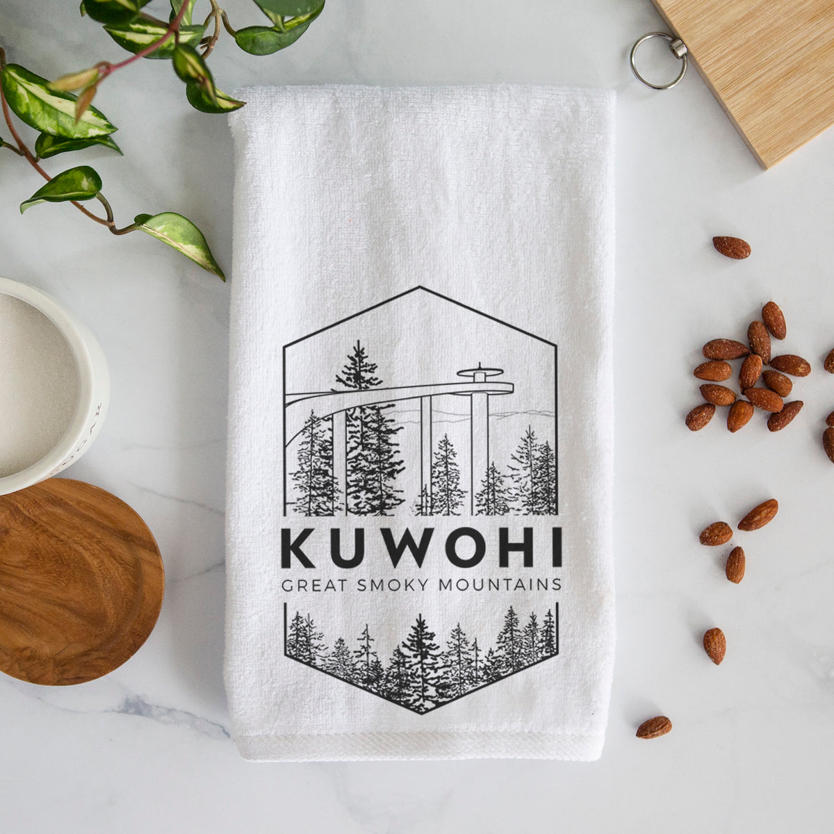 White hand towel printed with a black line art badge of the Kuwohi observation tower above pine trees, with the words Kuwohi, Great Smoky Mountains.