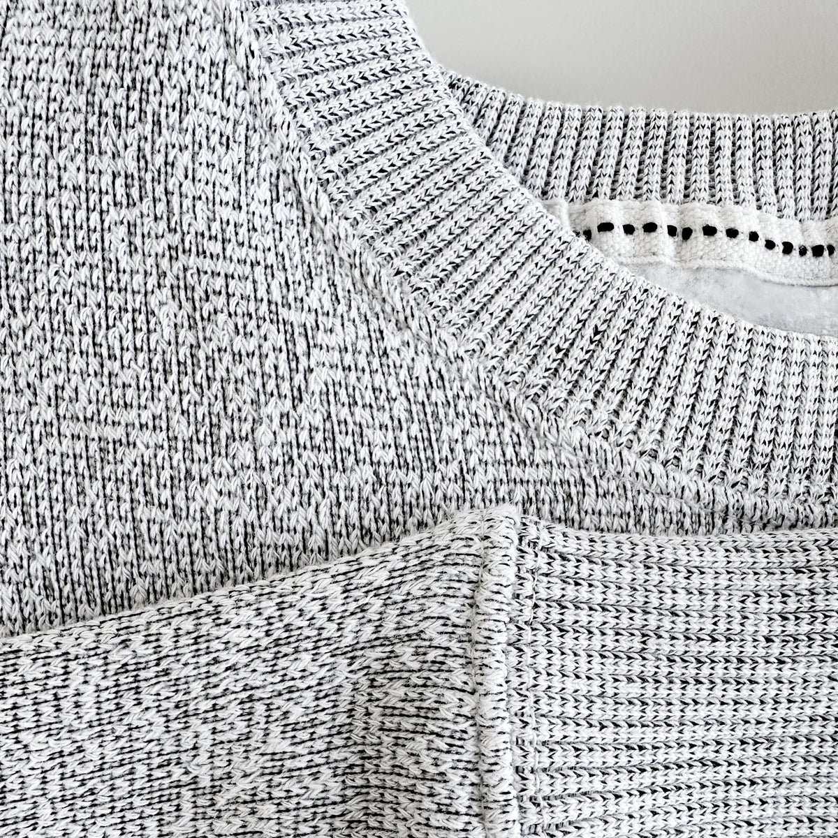 Close-up of a heather grey knit sweatshirt, showing the speckled knit texture and ribbed collar.