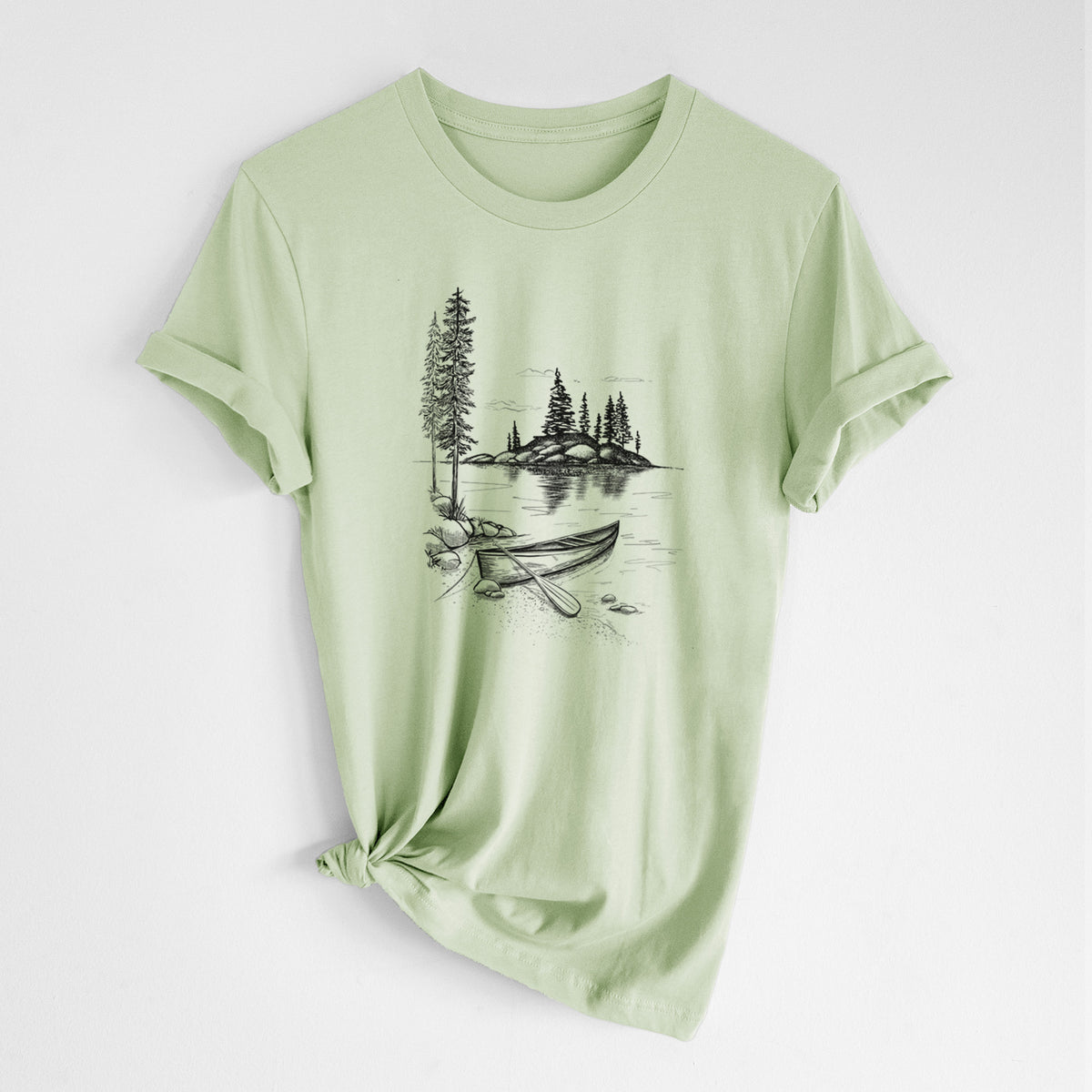 Spring green lightweight cotton t-shirt laid flat with the sleeves rolled, printed with a black ink illustration of a canoe resting on the shore of a lake with pine trees on a small island.
