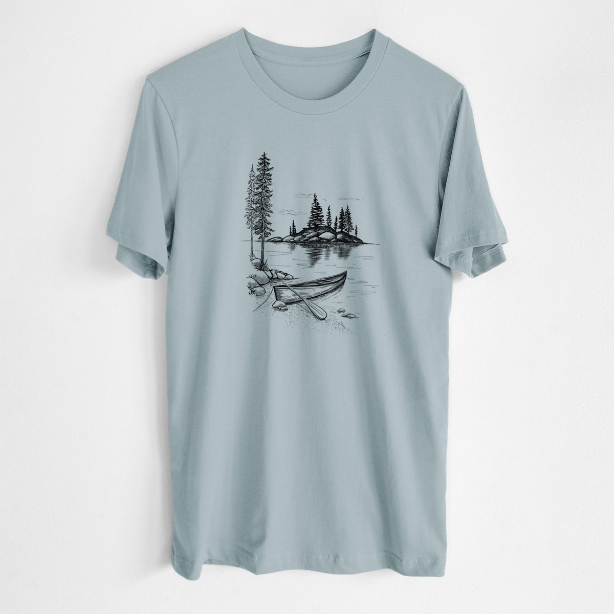 Vintage denim lightweight cotton t-shirt laid flat, printed with a black ink illustration of a canoe resting on the shore of a lake with pine trees on a small island.