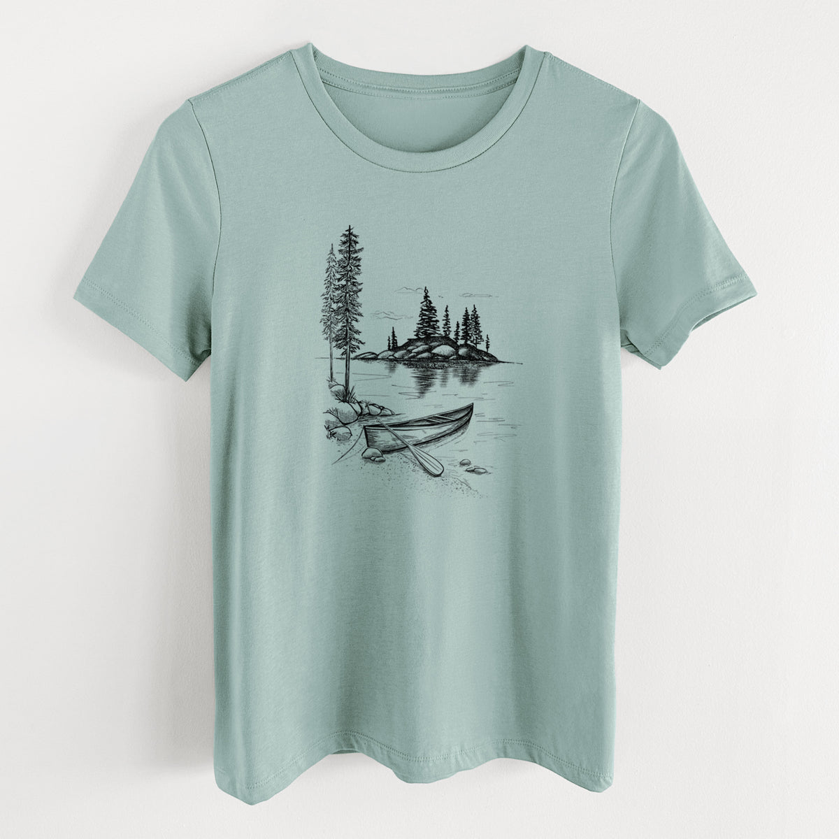Dusty blue women's relaxed fit cotton t-shirt laid flat, printed with a black ink illustration of a canoe resting on the shore of a lake with pine trees on a small island.