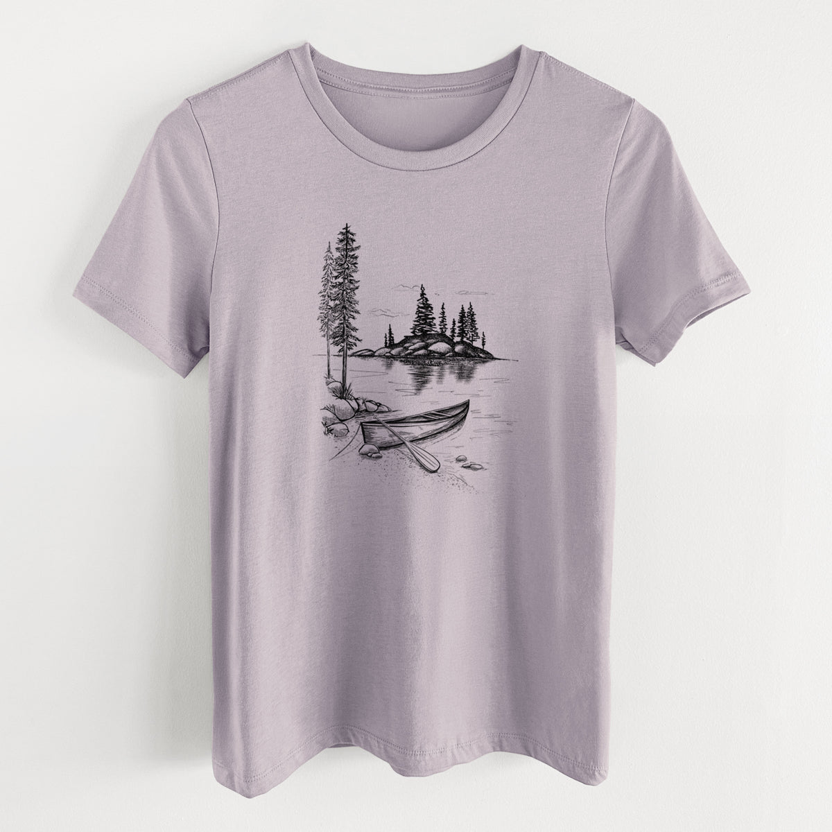 Light violet women's relaxed fit cotton t-shirt laid flat, printed with a black ink illustration of a canoe resting on the shore of a lake with pine trees on a small island.