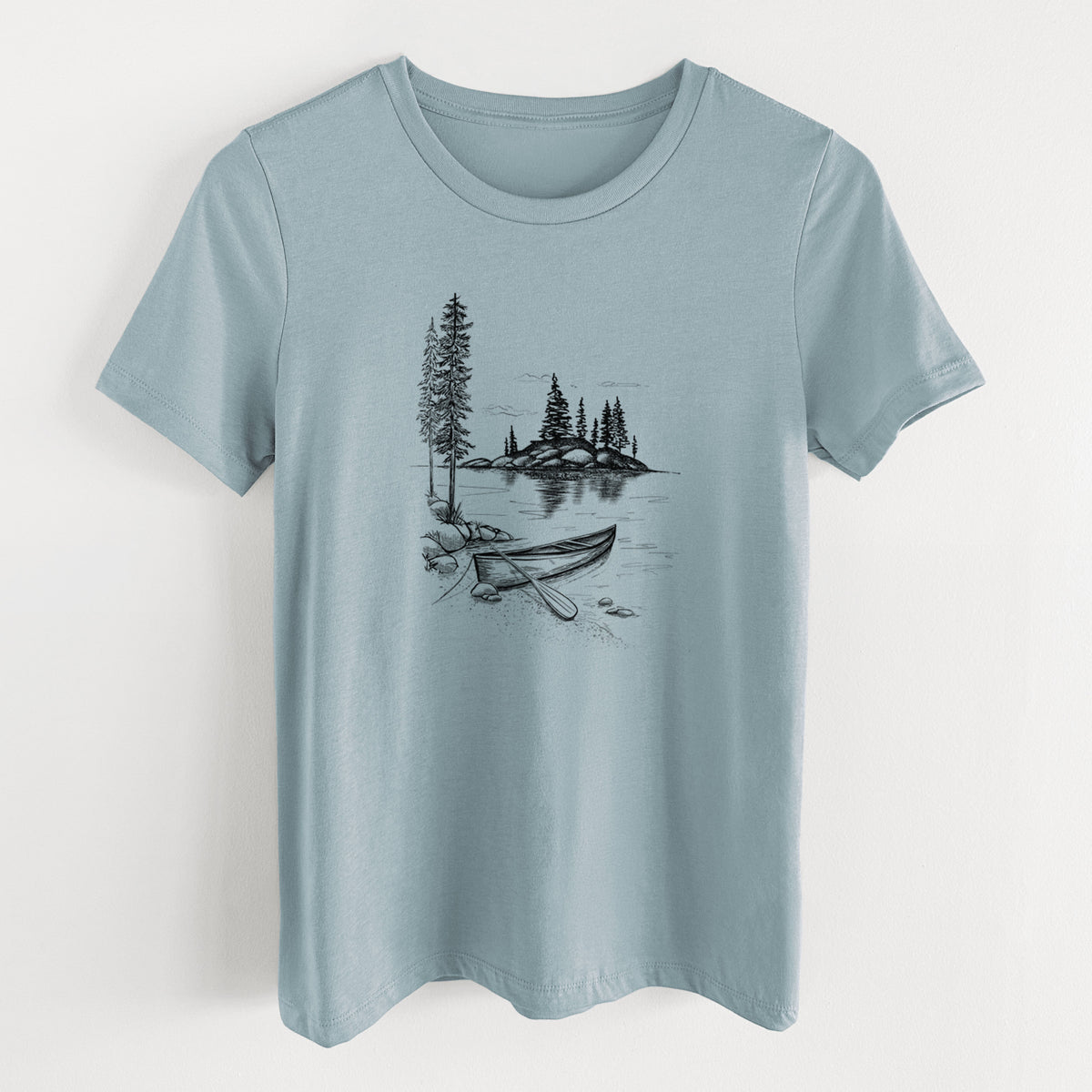 Vintage denim women's relaxed fit cotton t-shirt laid flat, printed with a black ink illustration of a canoe resting on the shore of a lake with pine trees on a small island.