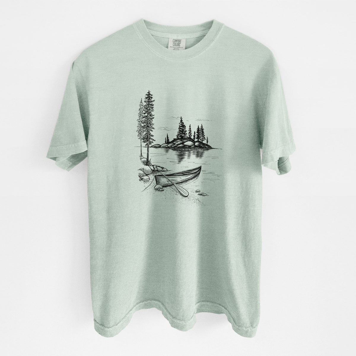 Bay green Comfort Colors t-shirt laid flat, printed with a black ink illustration of a canoe resting on the shore of a lake with pine trees on a small island.
