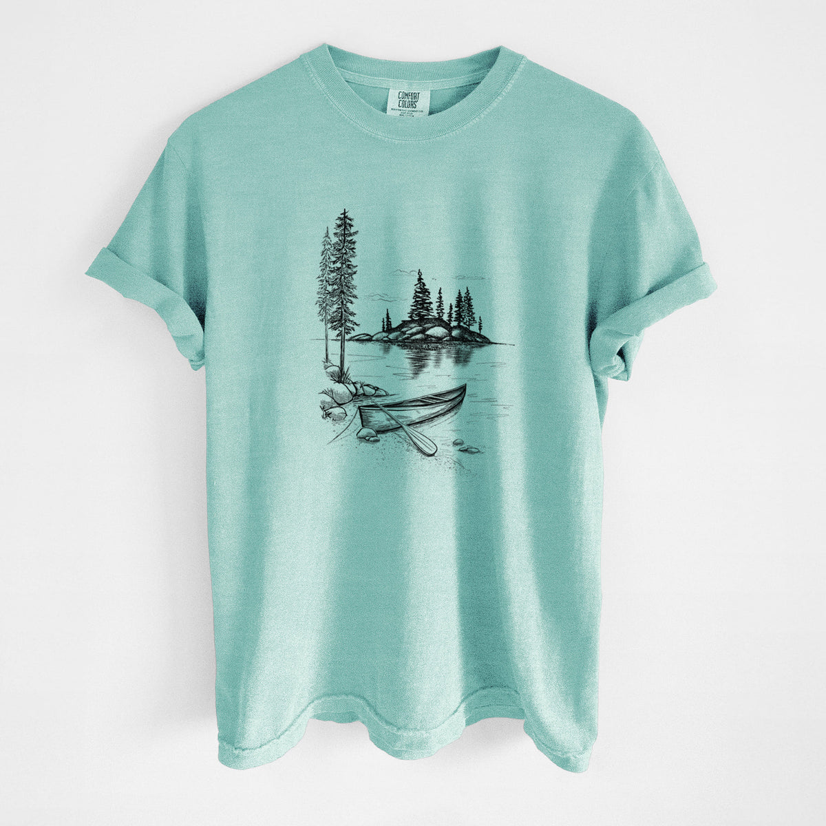 Chalky mint Comfort Colors t-shirt laid flat, printed with a black ink illustration of a canoe resting on the shore of a lake with pine trees on a small island.