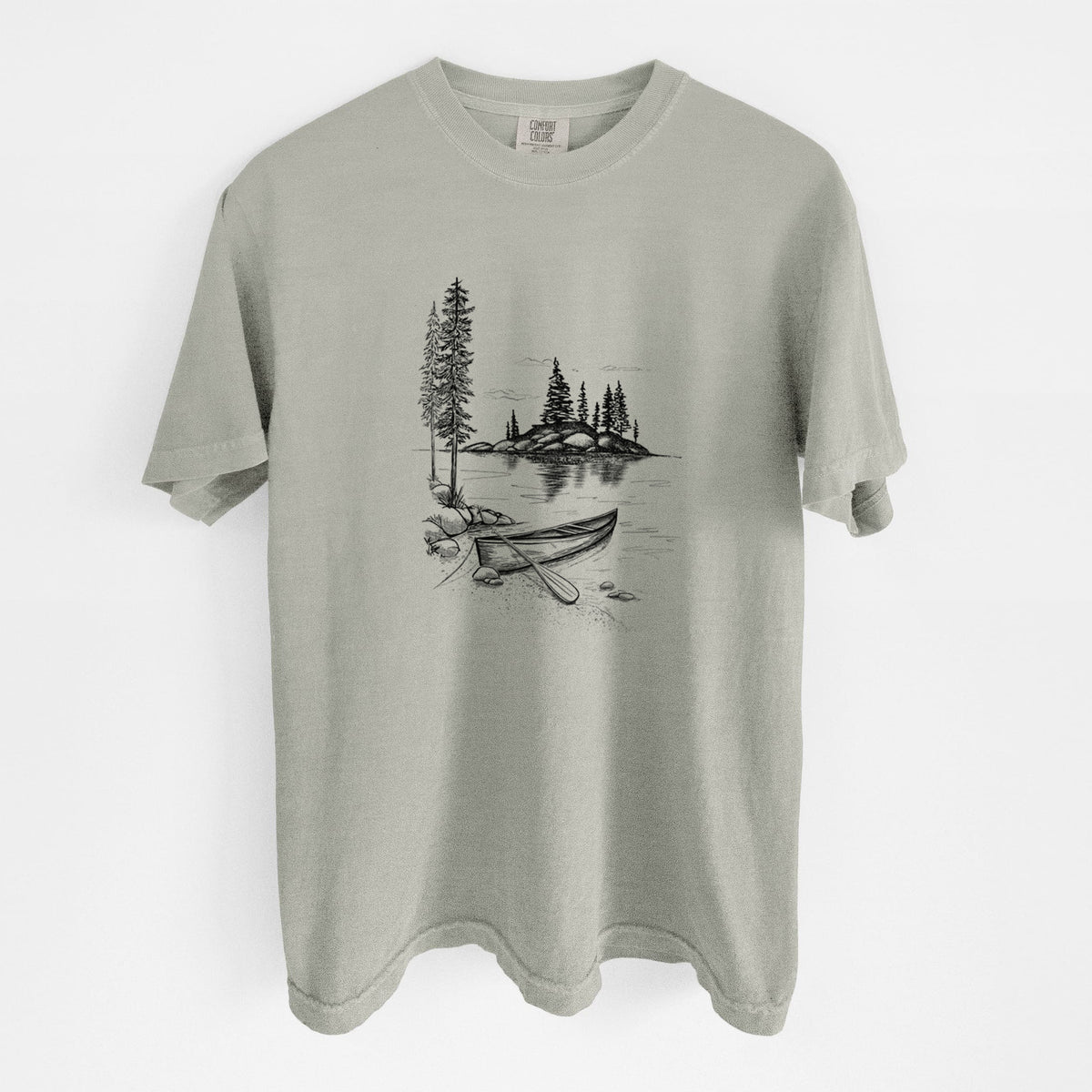 Sandstone beige Comfort Colors t-shirt laid flat, printed with a black ink illustration of a canoe resting on the shore of a lake with pine trees on a small island.