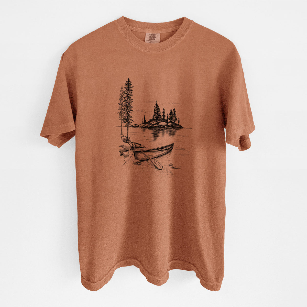 Yam burnt orange Comfort Colors t-shirt laid flat, printed with a black ink illustration of a canoe resting on the shore of a lake with pine trees on a small island.