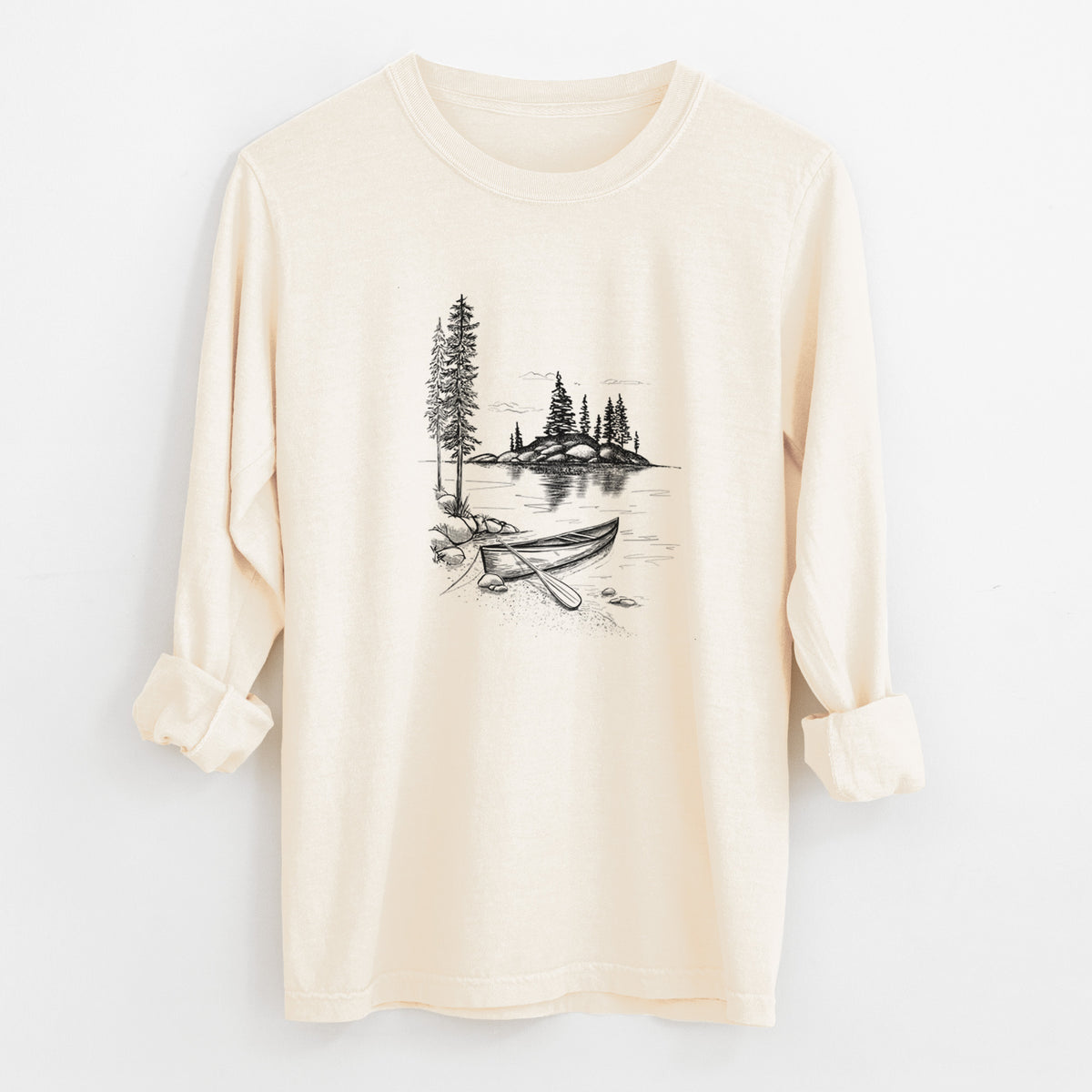 Ivory Comfort Colors long sleeve shirt laid flat with the cuffs rolled, printed with a black ink illustration of a canoe resting on the shore of a lake with pine trees on a small island.