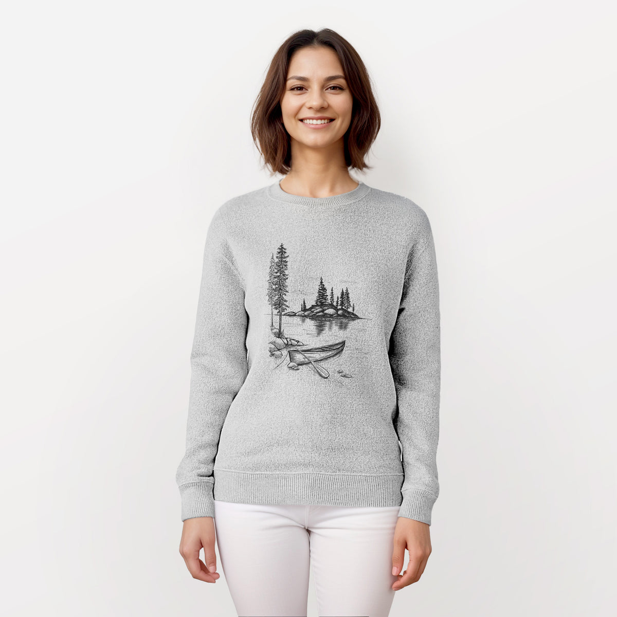Woman wearing a knit sweatshirt printed with a black ink illustration of a canoe resting on the shore of a lake with pine trees on a small island.