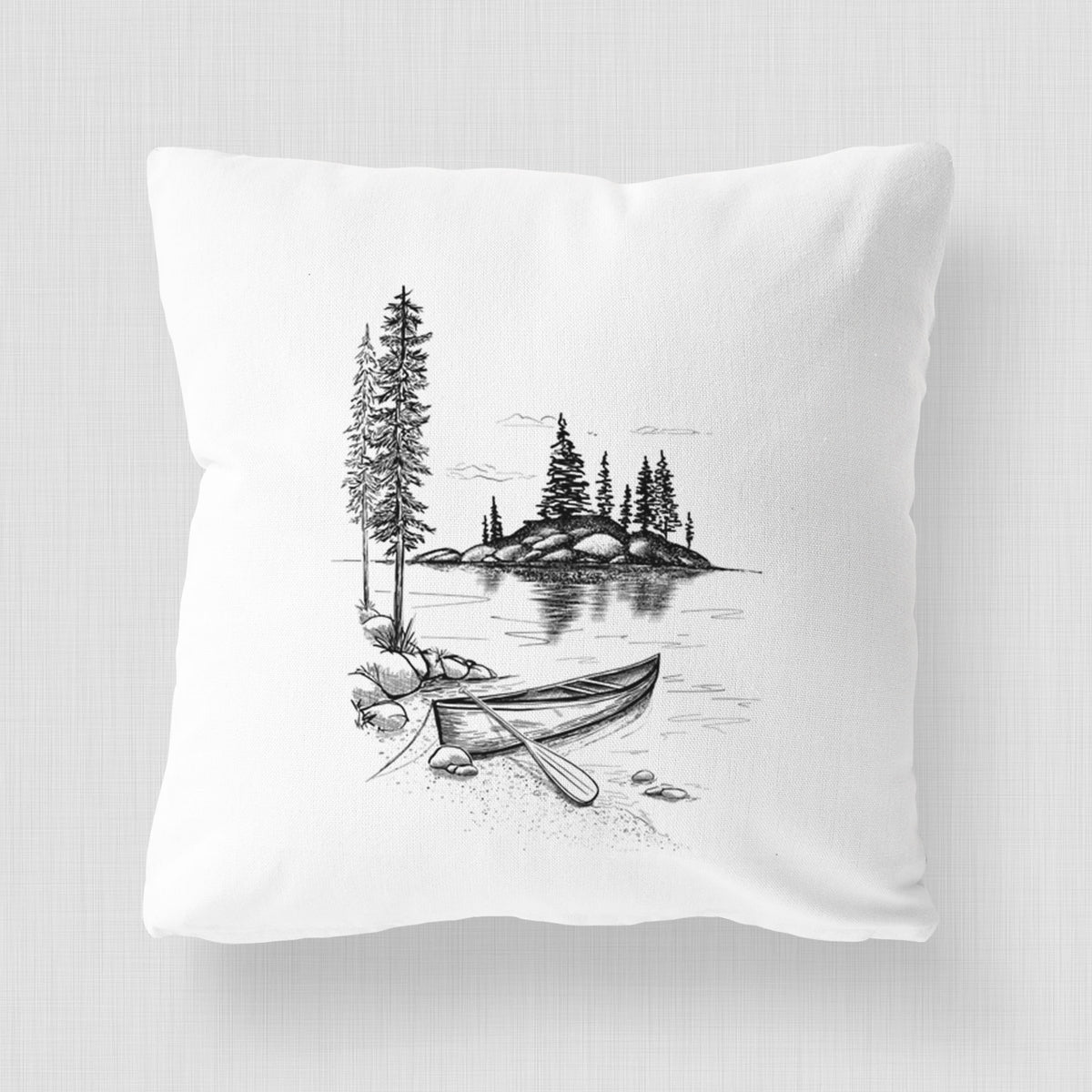 White pillow cover printed with a black ink illustration of a canoe resting on the shore of a lake with pine trees on a small island.