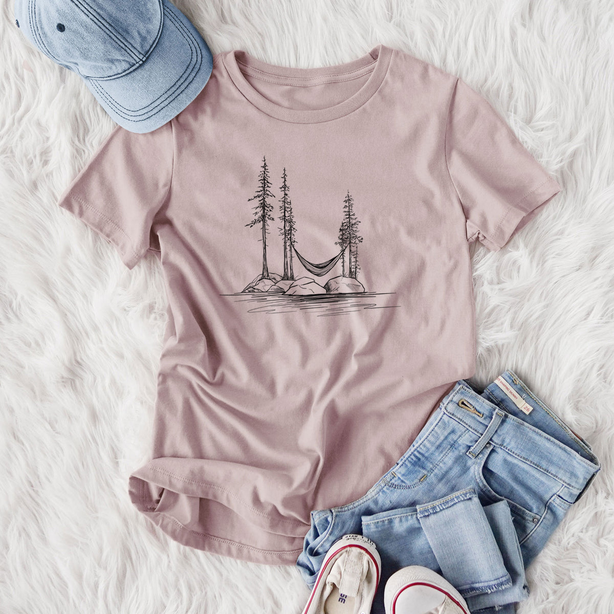 Women's relaxed fit cotton t-shirt printed with a black ink illustration of a hammock strung between pine trees on a small lakeside island, styled flat on a white faux fur rug with jeans.