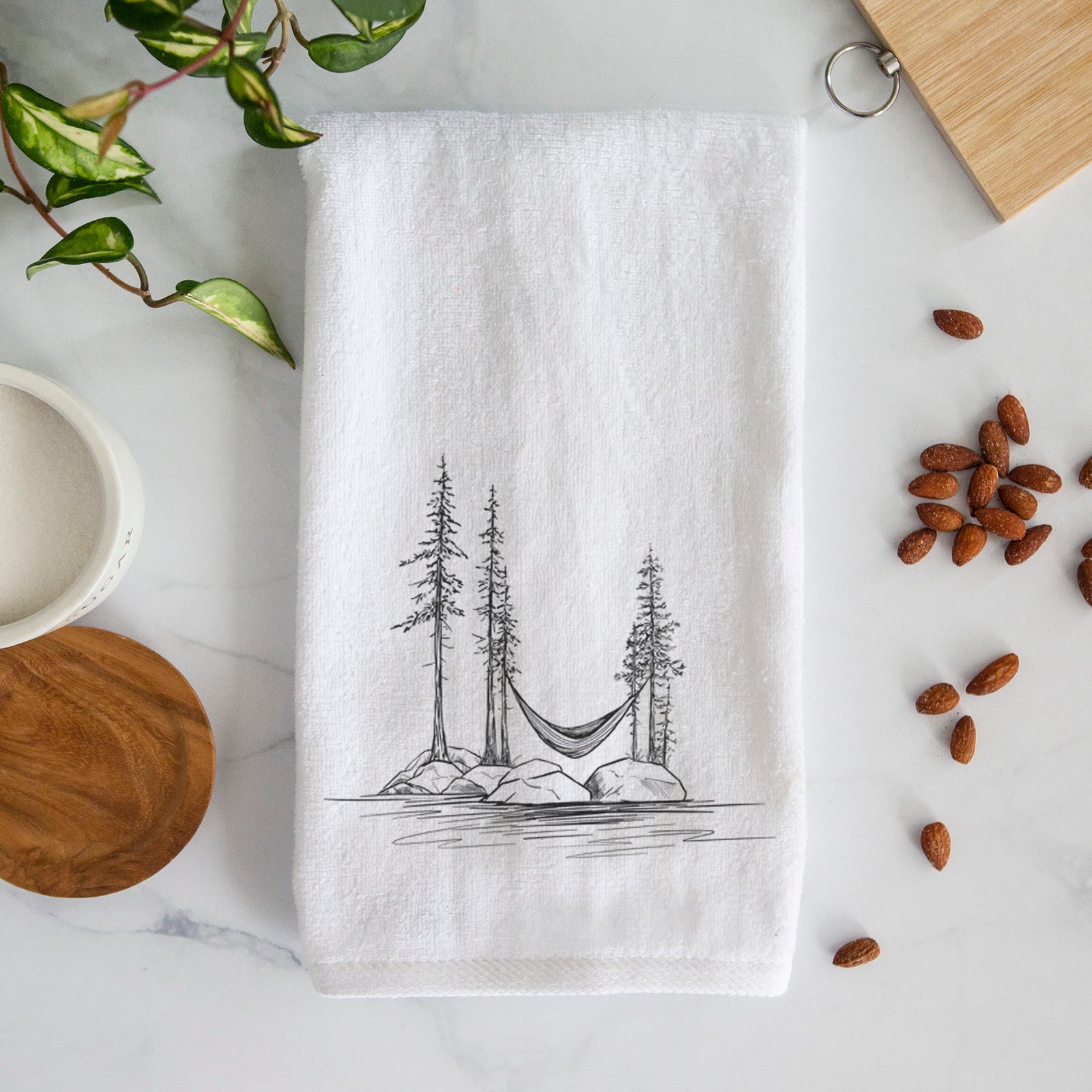 White hand towel printed with a black ink illustration of a hammock strung between pine trees on a small lakeside island.
