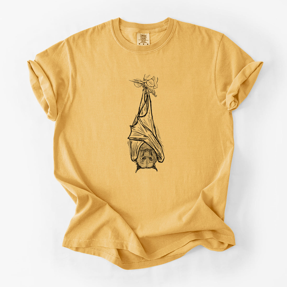 Golden wheat yellow Comfort Colors t-shirt laid flat, printed with a black ink illustration of a large flying fox bat hanging upside down with its wings wrapped around it.