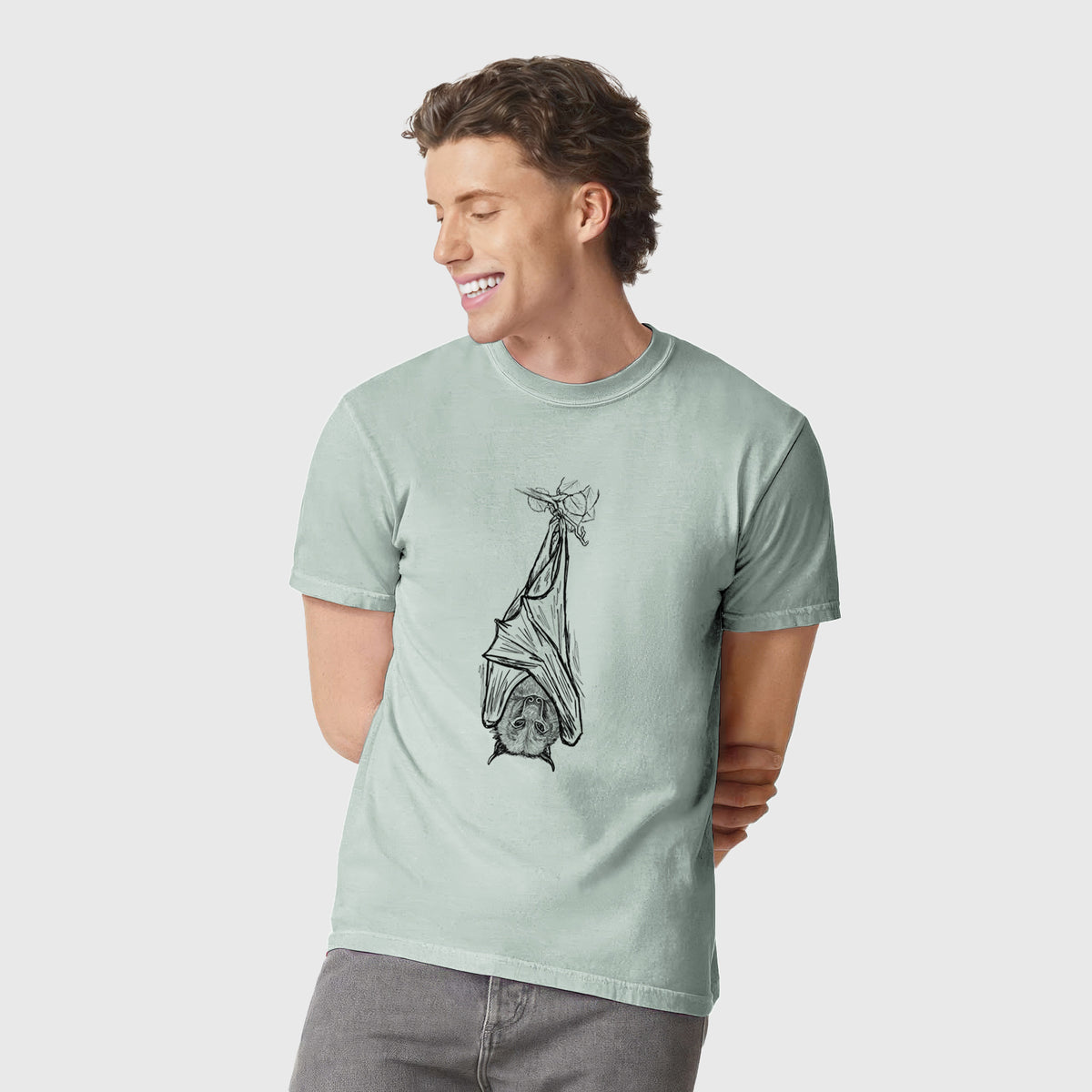 Man wearing a Comfort Colors t-shirt printed with a black ink illustration of a large flying fox bat hanging upside down with its wings wrapped around it.