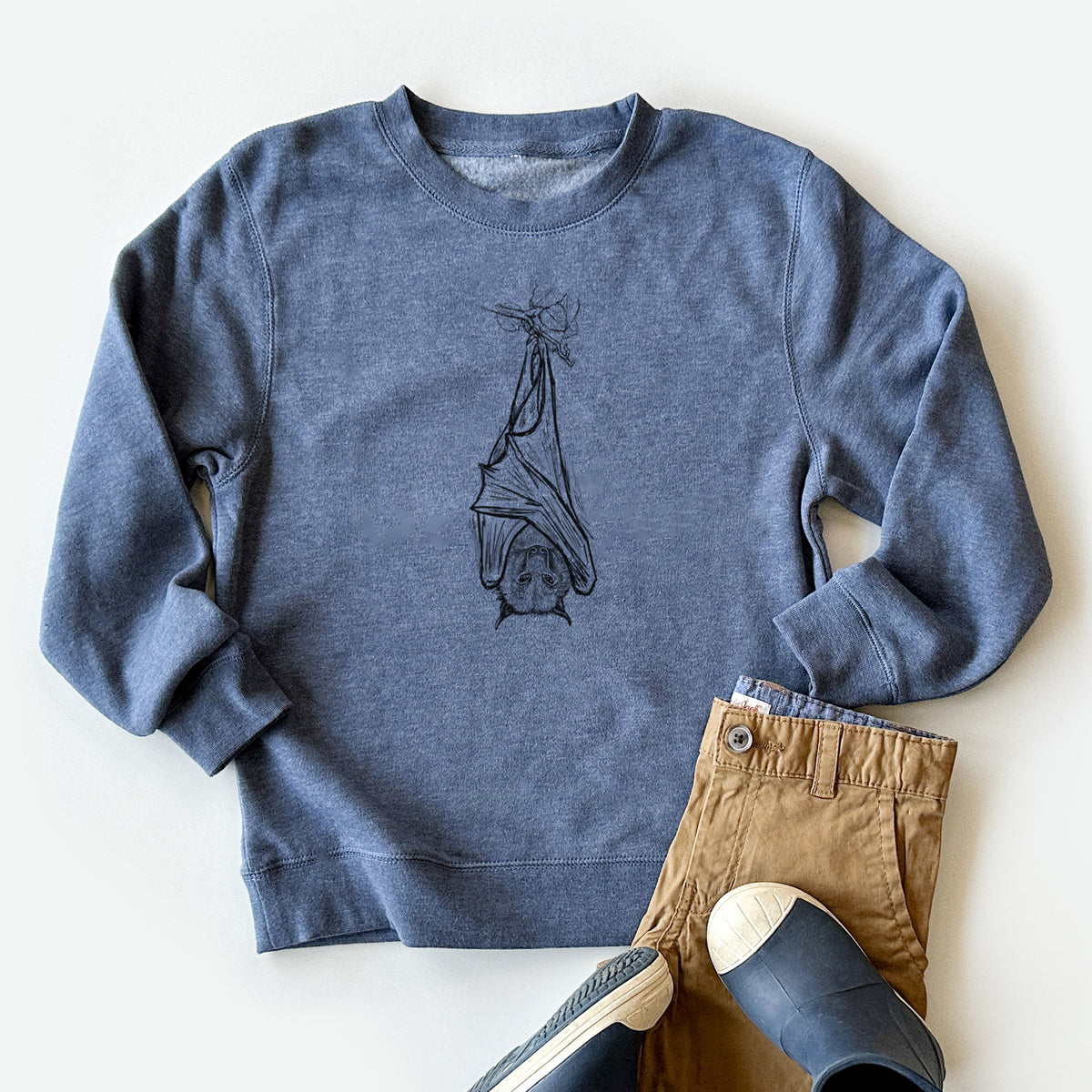 Youth crewneck sweatshirt printed with a black ink illustration of a large flying fox bat hanging upside down with its wings wrapped around it, styled flat with khaki pants and shoes.