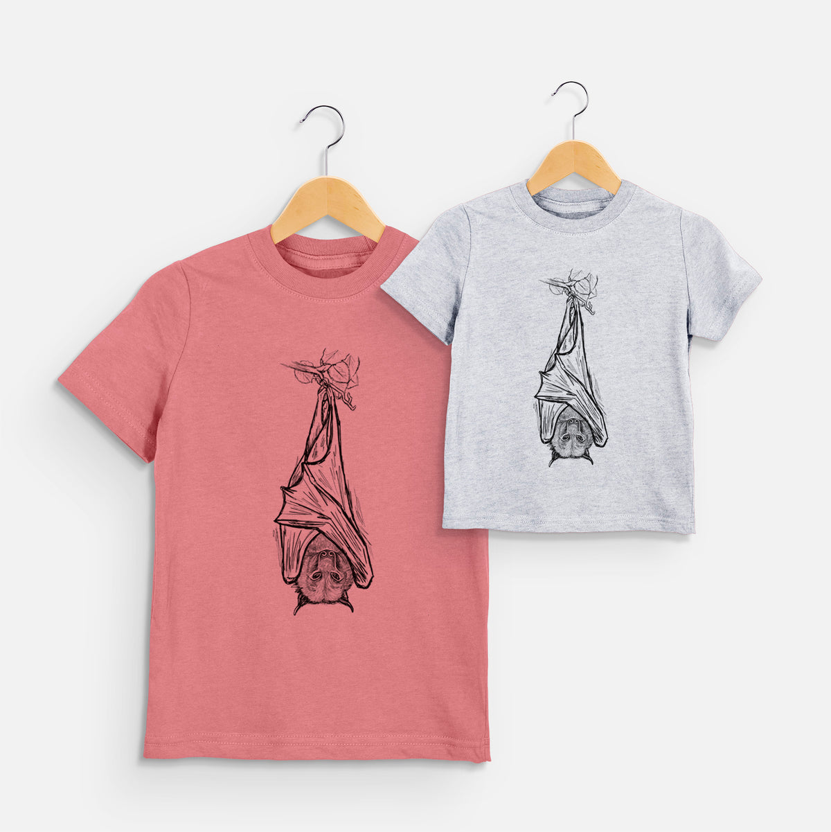 Two youth t-shirts in different colors on hangers, printed with a black ink illustration of a large flying fox bat hanging upside down with its wings wrapped around it.
