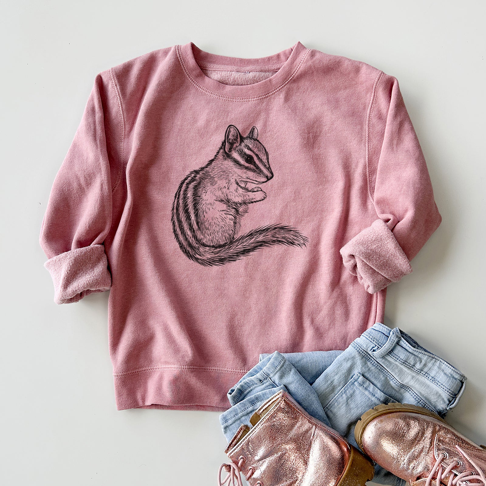Boy wearing a youth crewneck sweatshirt printed with a detailed black ink illustration of a least chipmunk sitting and holding food in its paws, outdoors.