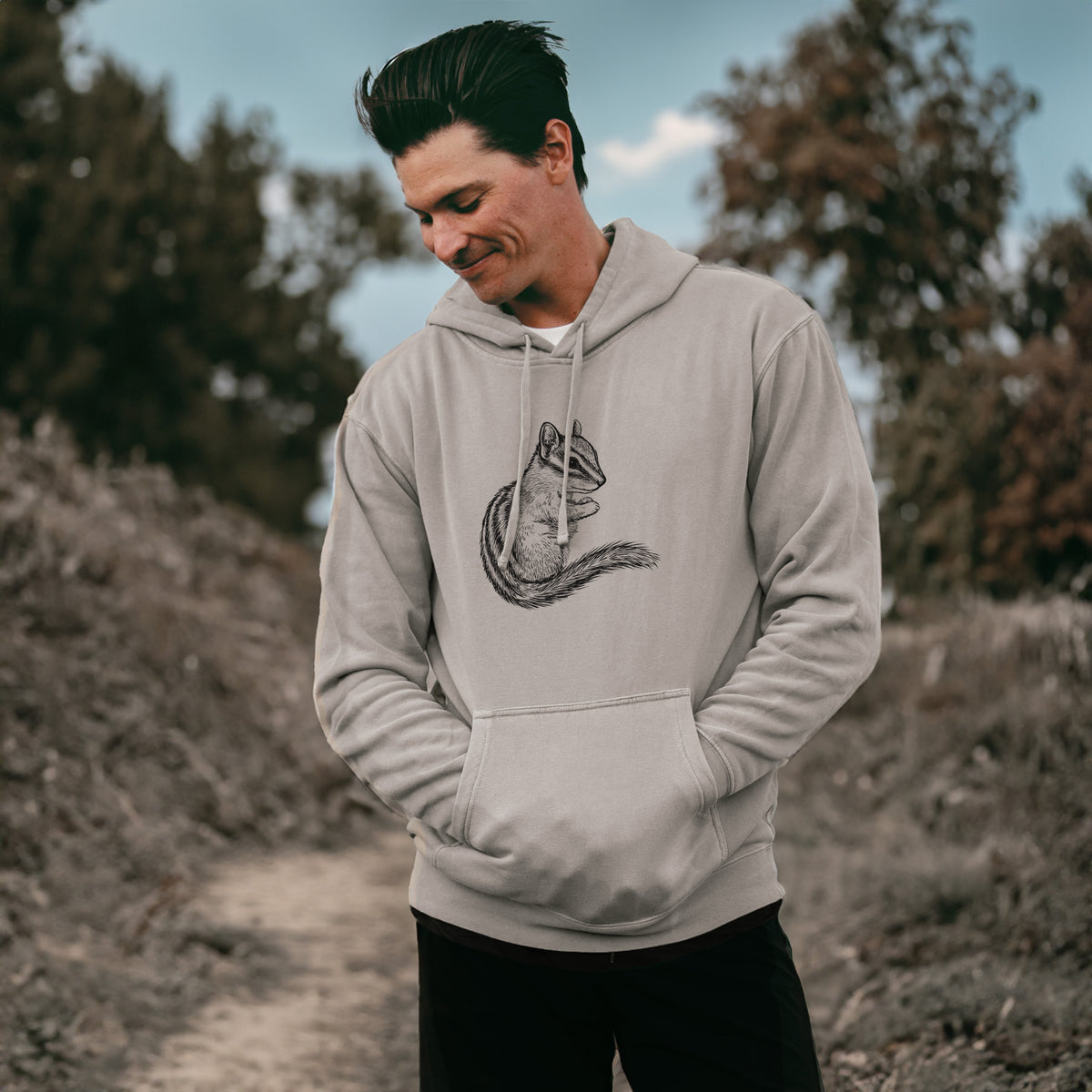 Man wearing a cement grey pigment dyed hoodie printed with a detailed black ink illustration of a least chipmunk sitting and holding food in its paws.