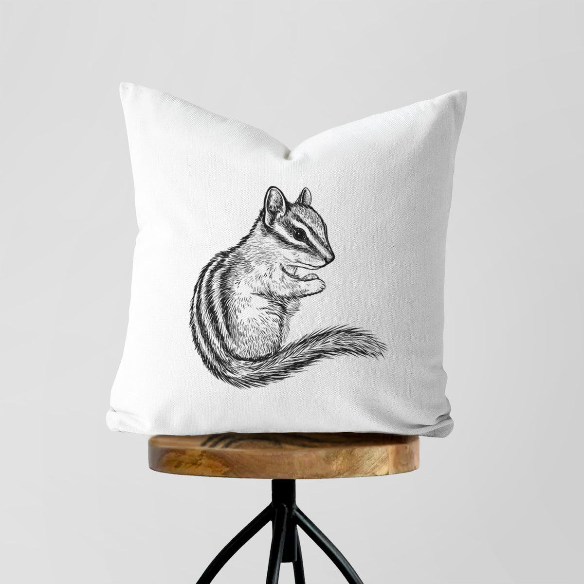 White pillow cover printed with a detailed black ink illustration of a least chipmunk sitting and holding food in its paws, on a wooden stool.