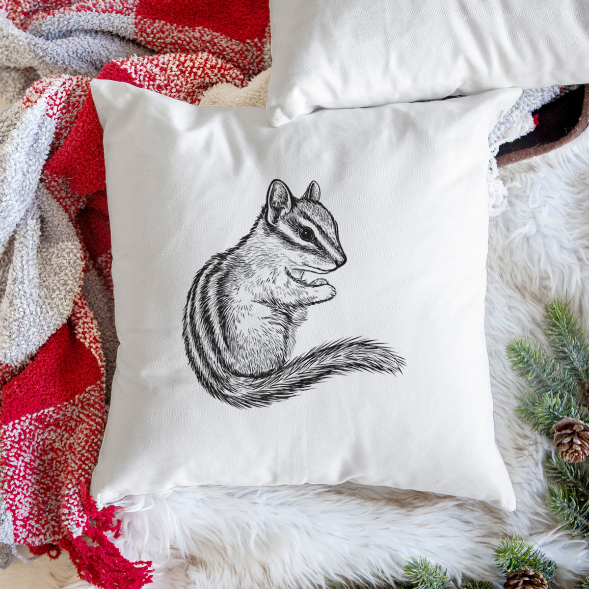 White pillow cover printed with a detailed black ink illustration of a least chipmunk sitting and holding food in its paws, on a woven chair.