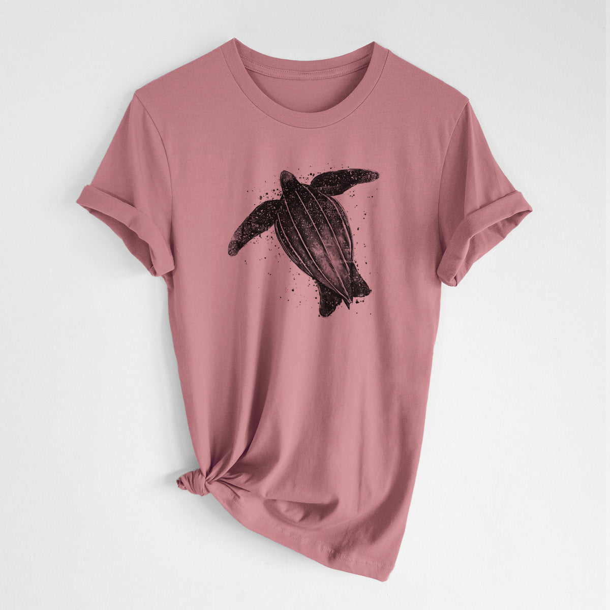 Mauve pink lightweight cotton t-shirt laid flat with the sleeves rolled, printed with a black ink illustration of a leatherback sea turtle swimming, with ink splatters.