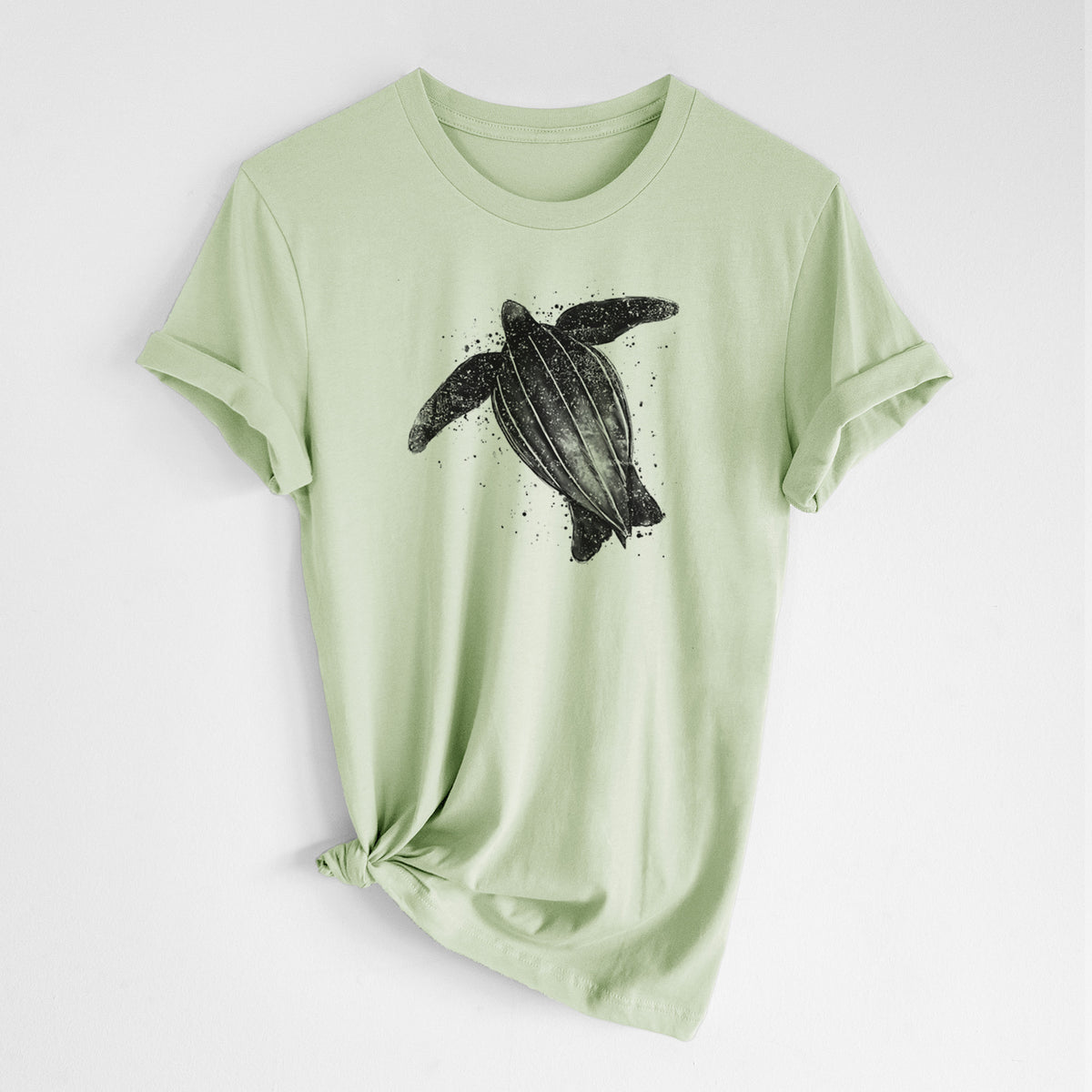 Spring green lightweight cotton t-shirt laid flat with the sleeves rolled, printed with a black ink illustration of a leatherback sea turtle swimming, with ink splatters.