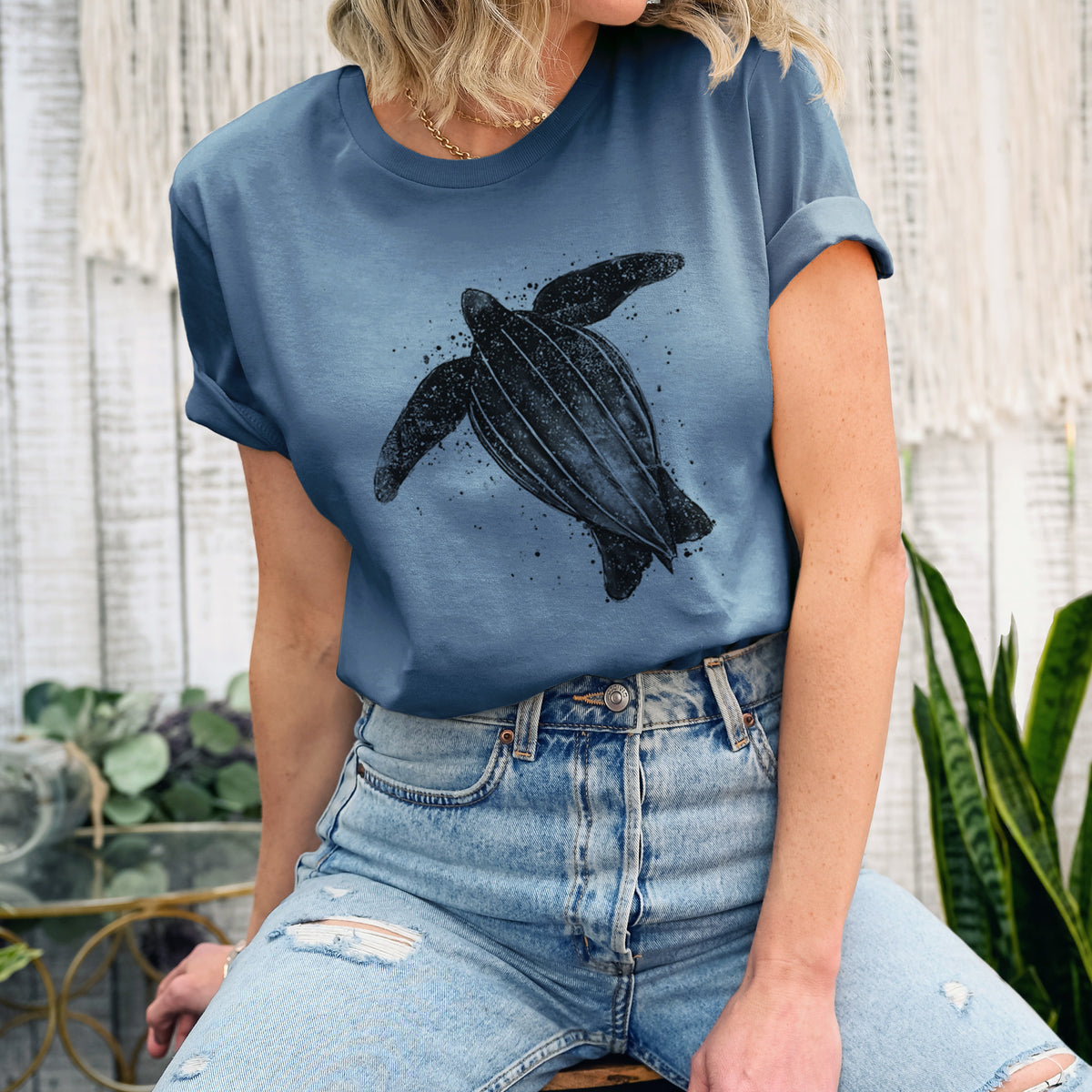 Woman wearing a steel blue lightweight cotton t-shirt printed with a black ink illustration of a leatherback sea turtle swimming, with ink splatters.