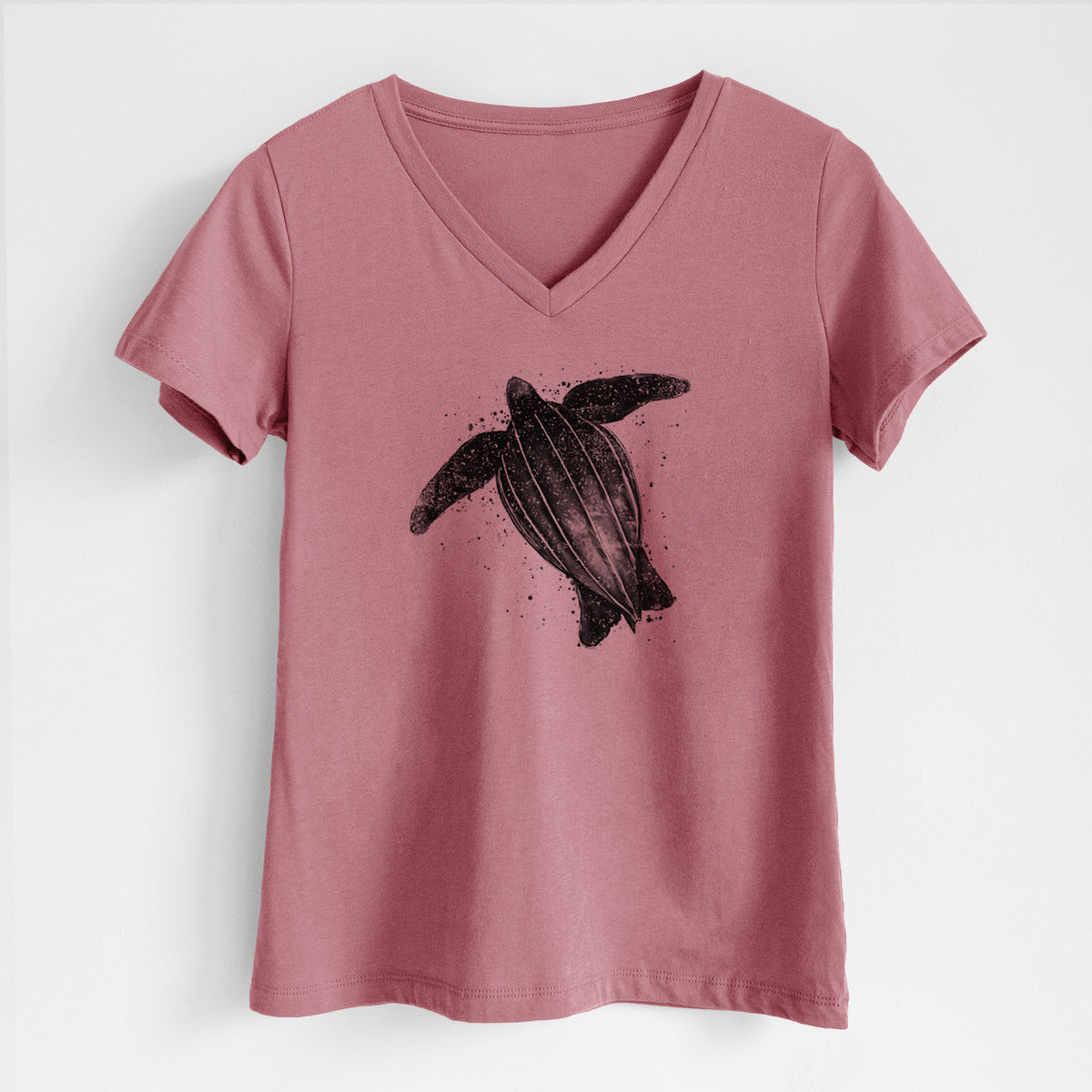 Mauve pink women's relaxed fit cotton V-neck t-shirt laid flat, printed with a black ink illustration of a leatherback sea turtle swimming, with ink splatters.