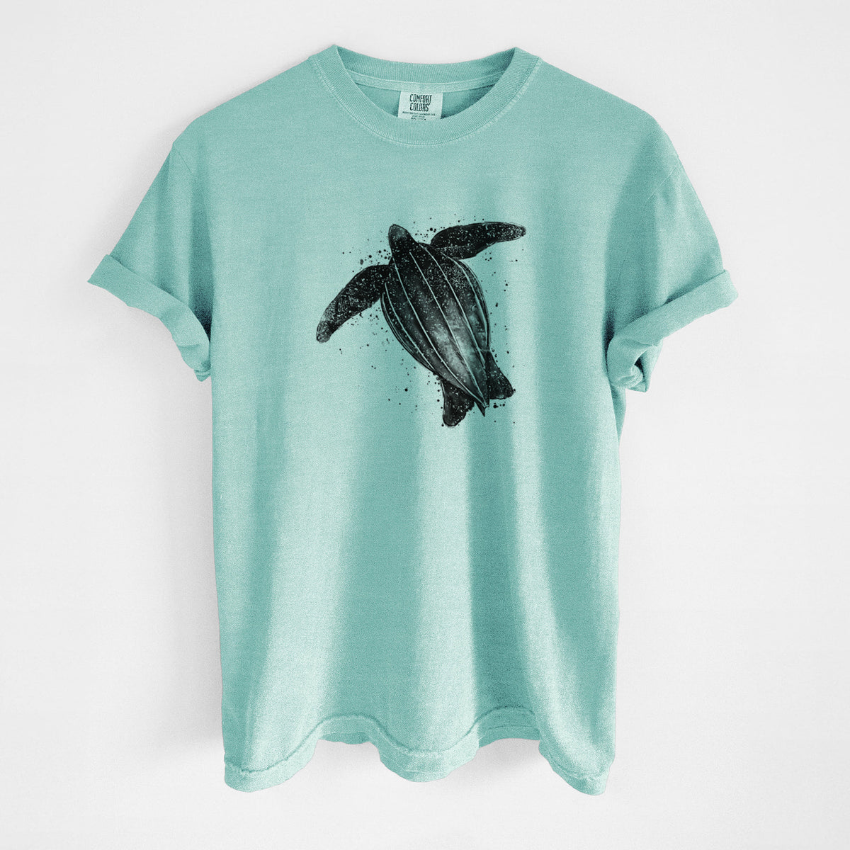 Chalky mint Comfort Colors t-shirt laid flat, printed with a black ink illustration of a leatherback sea turtle swimming, with ink splatters.
