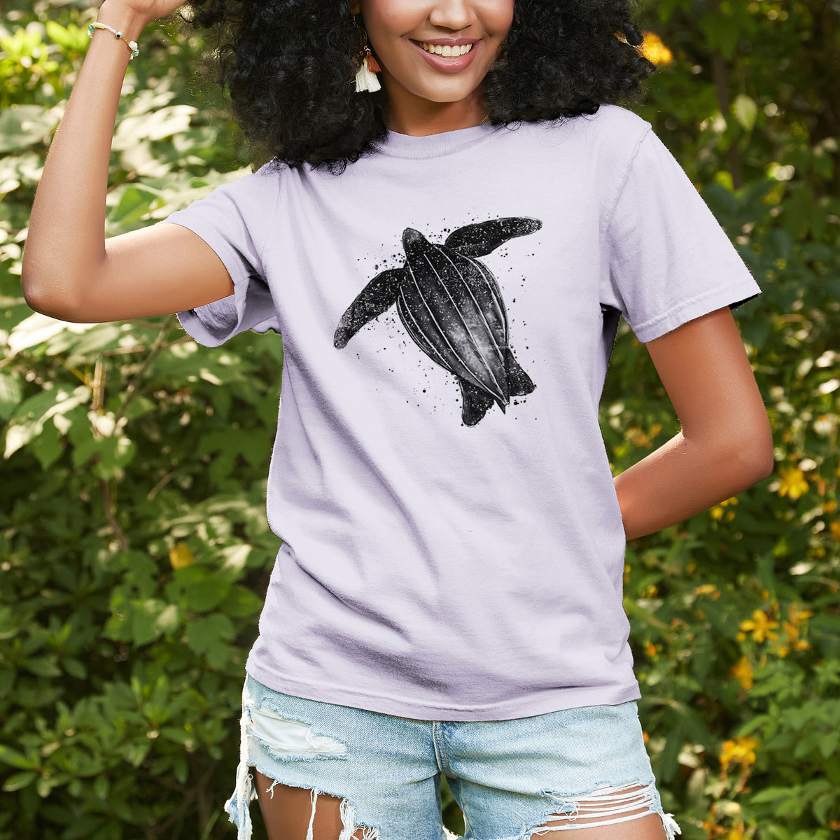 Woman wearing a Comfort Colors t-shirt printed with a black ink illustration of a leatherback sea turtle swimming, with ink splatters, outdoors.