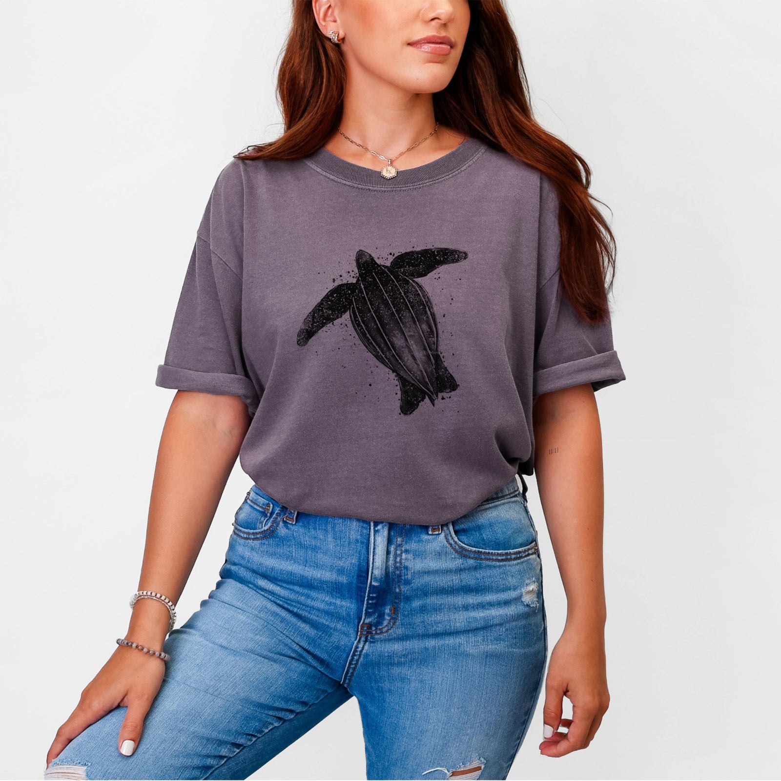 Blue jean Comfort Colors t-shirt laid flat, printed with a black ink illustration of a leatherback sea turtle swimming, with ink splatters.