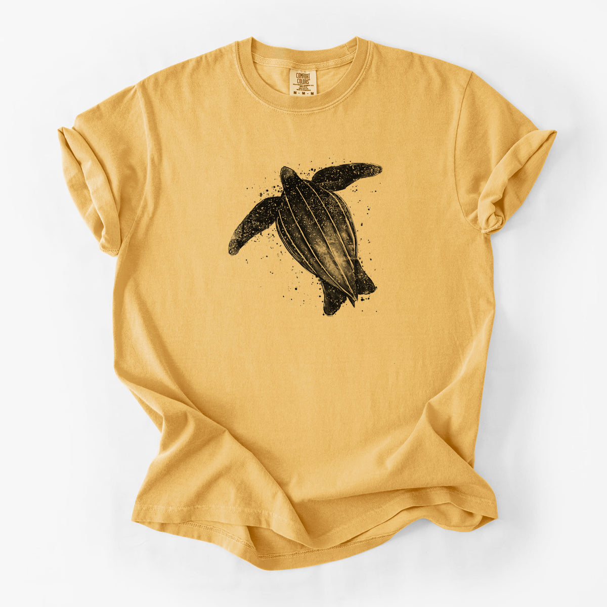Golden wheat yellow Comfort Colors t-shirt laid flat, printed with a black ink illustration of a leatherback sea turtle swimming, with ink splatters.