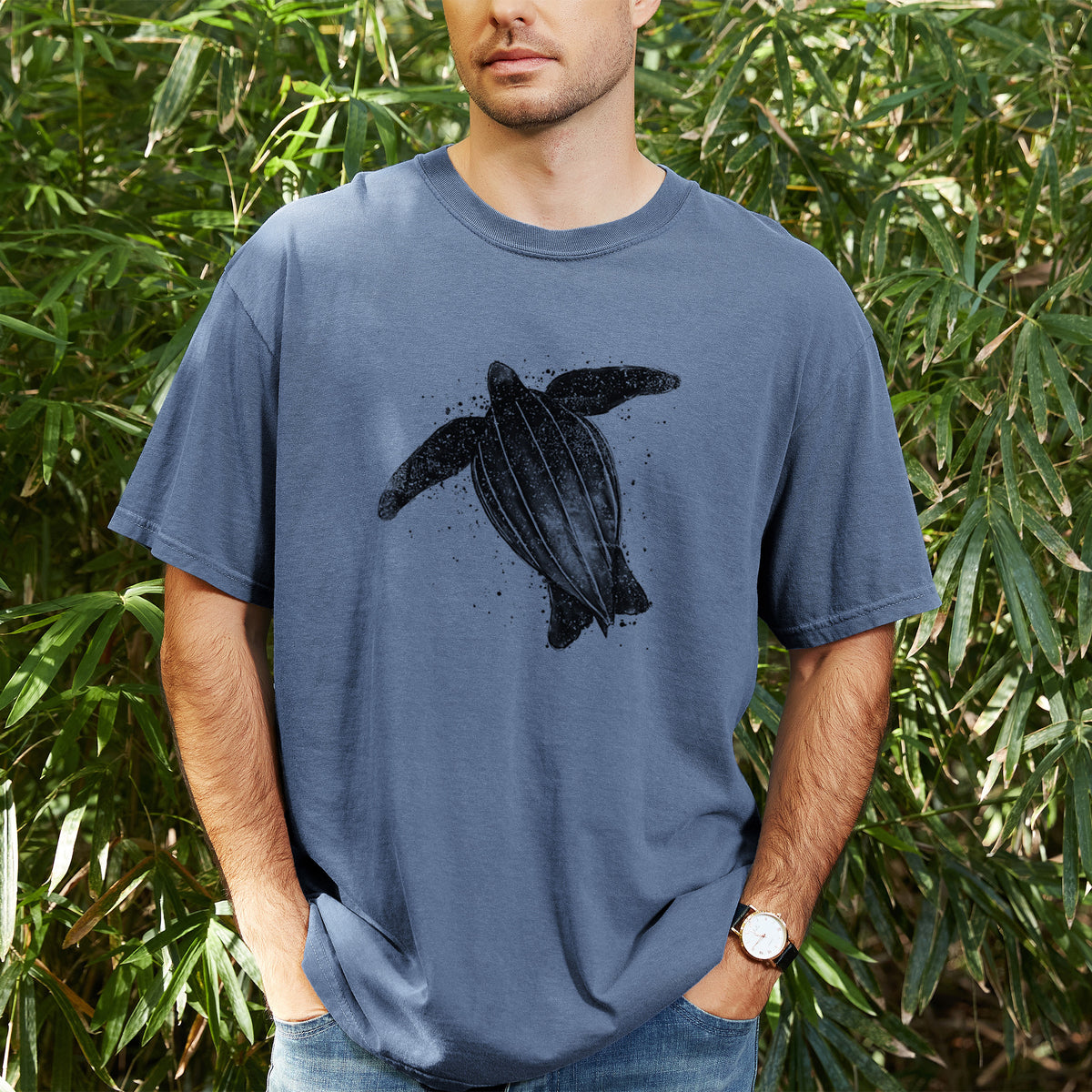 Man wearing a Comfort Colors t-shirt printed with a black ink illustration of a leatherback sea turtle swimming, with ink splatters, outdoors.