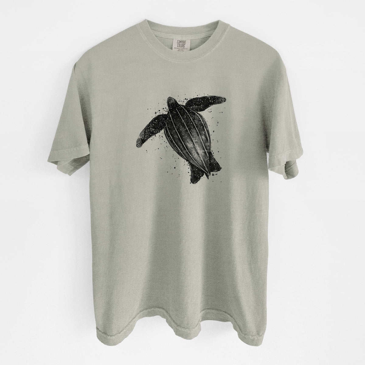 Sandstone beige Comfort Colors t-shirt laid flat, printed with a black ink illustration of a leatherback sea turtle swimming, with ink splatters.