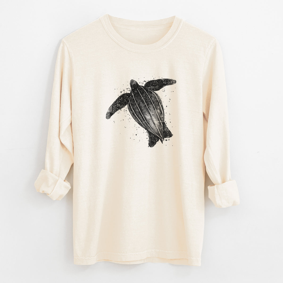 Ivory Comfort Colors long sleeve shirt laid flat with the cuffs rolled, printed with a black ink illustration of a leatherback sea turtle swimming, with ink splatters.