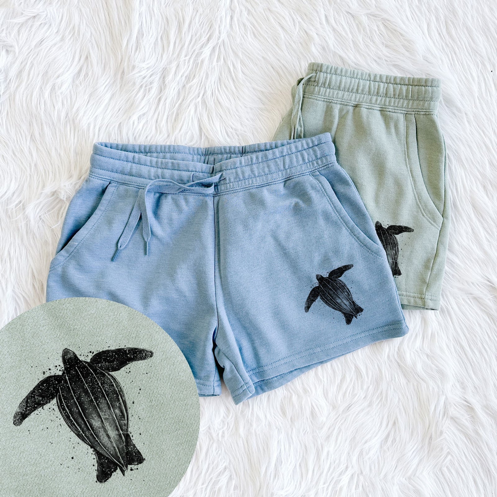 Two pairs of Cali Wave shorts in different colors printed with a black ink illustration of a leatherback sea turtle swimming, with ink splatters, with a close-up of the print.