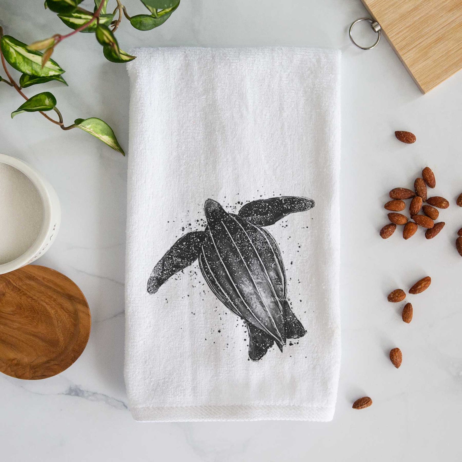 White hand towel printed with a black ink illustration of a leatherback sea turtle swimming, with ink splatters.