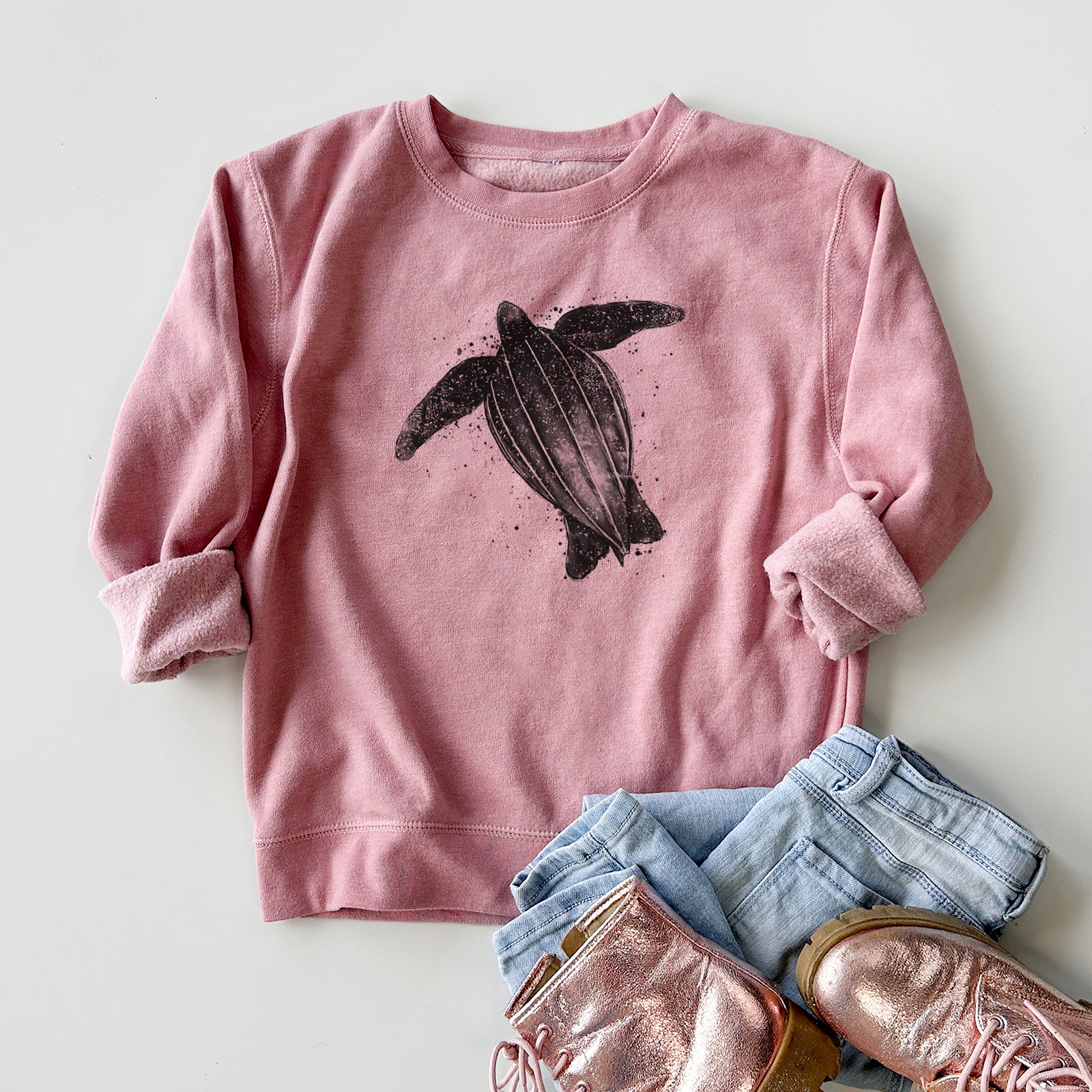 Boy wearing a youth crewneck sweatshirt printed with a black ink illustration of a leatherback sea turtle swimming, with ink splatters, outdoors.
