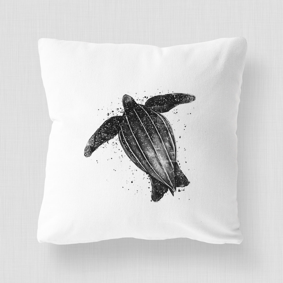 White pillow cover printed with a black ink illustration of a leatherback sea turtle swimming, with ink splatters.